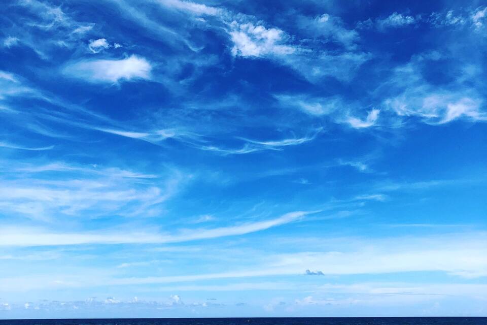 A clear blue sky with scattered clouds over the ocean.