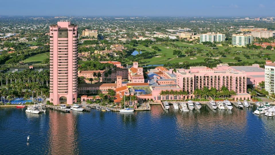 A coastal cityscape with a prominent pink tower, marina, and surrounding residential and commercial buildings.