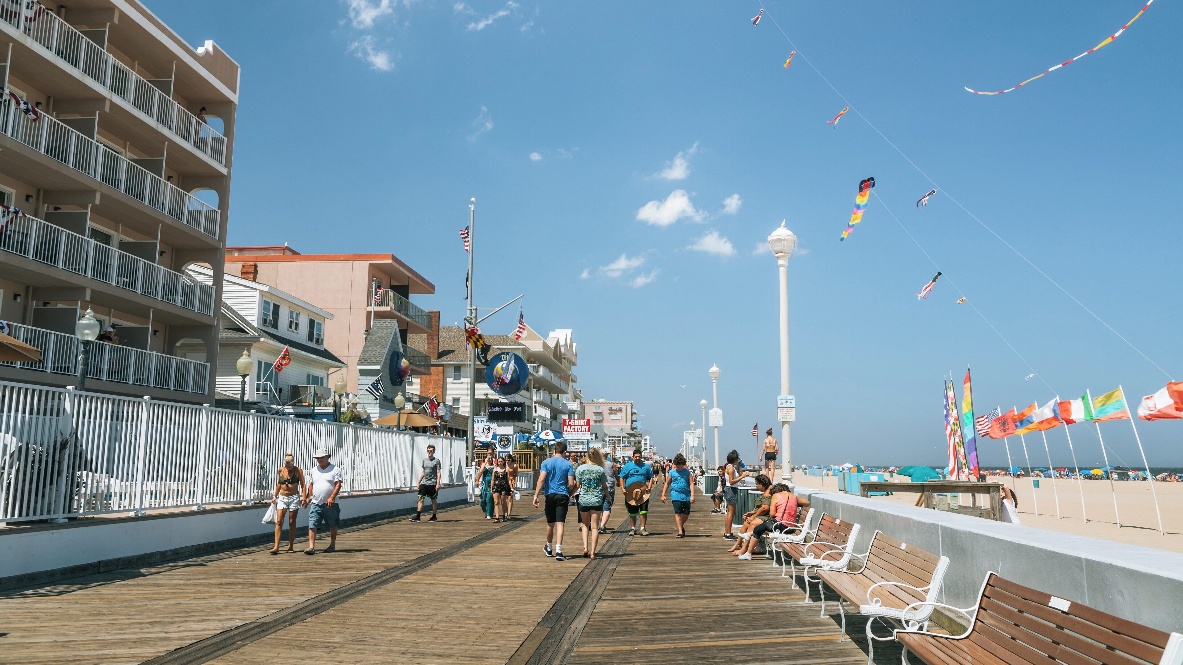 Visitors enjoying a sunny day along the boardwalk in Downtown Ocean City, Maryland with shops and beach views