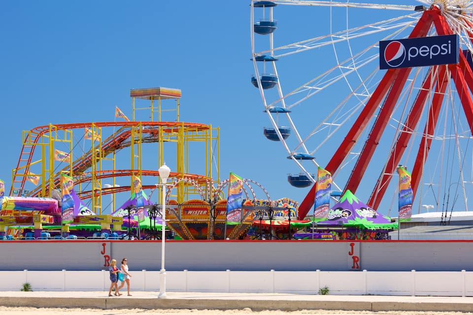 A vibrant amusement park with a large red Ferris wheel, a yellow roller coaster, and various colorful rides.