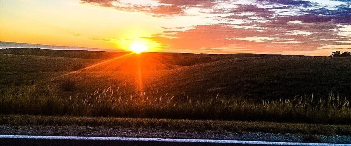 A sunset over a grassy hill with a road in the foreground.