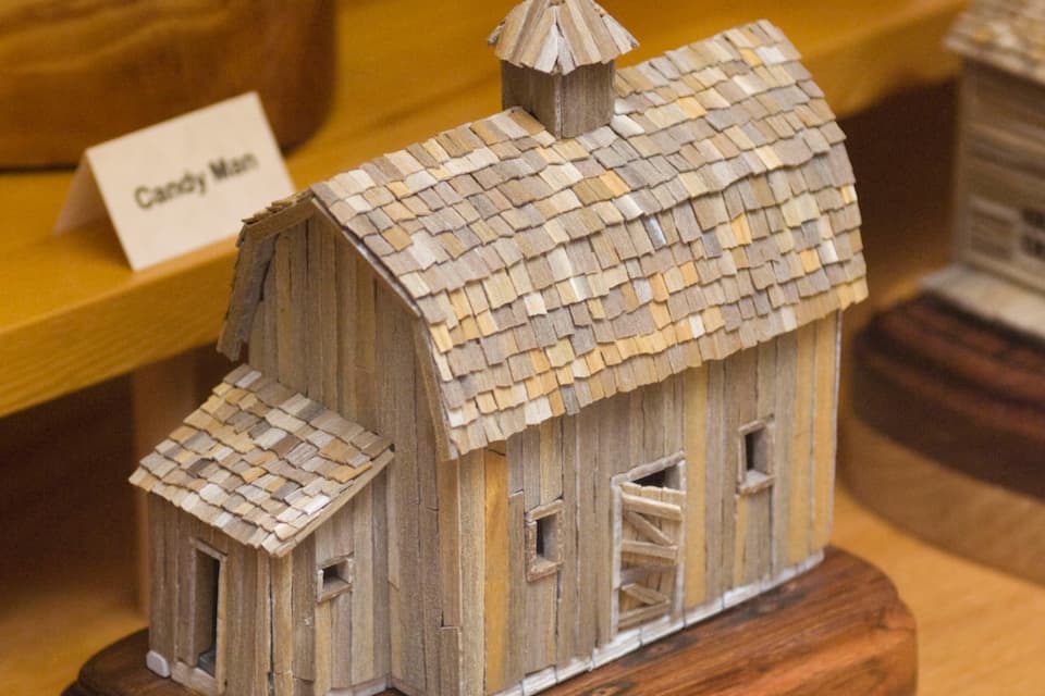 A wooden model of a rustic barn with a shingled roof and a small attached shed.
