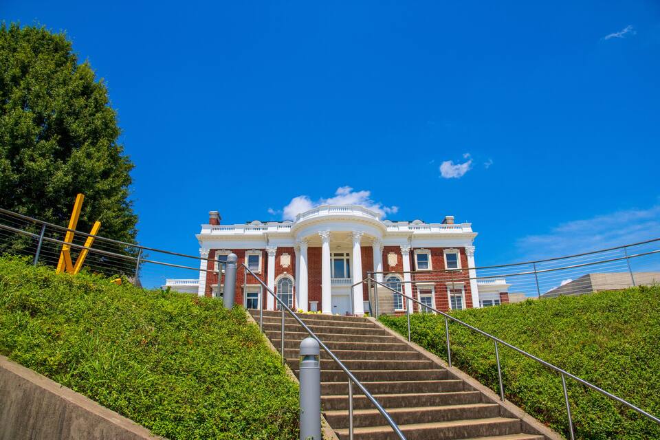 A grand building with a central dome, surrounded by lush greenery and a clear blue sky.