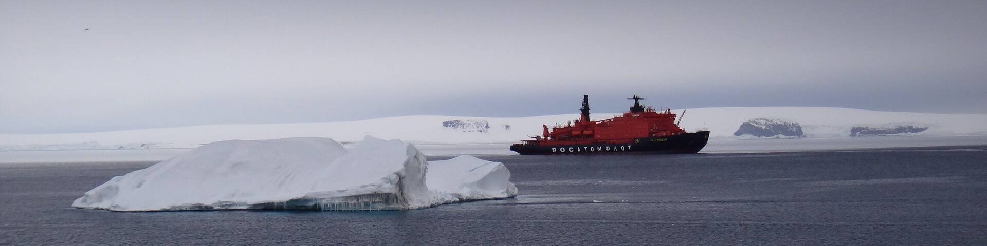 Un barco rojo llamado DOCATOMOTOT en aguas heladas con icebergs cubiertos de nieve al fondo.