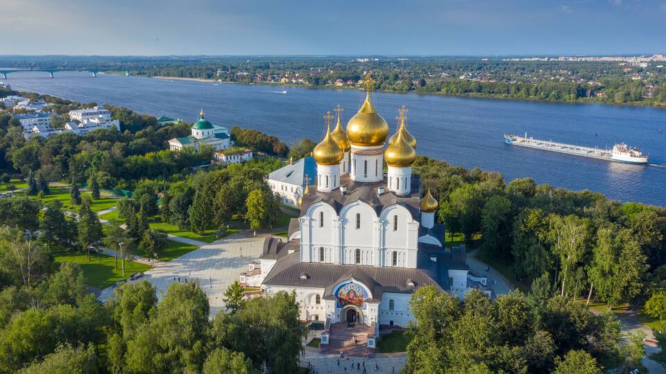 A large white church with golden domes, a river, and a cruise ship in the background.