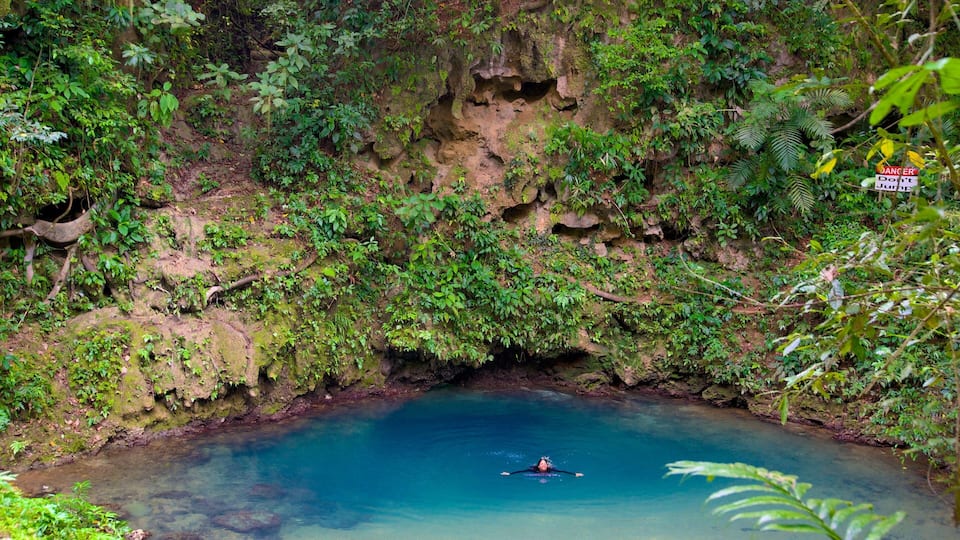 A person kayaking in a clear blue river surrounded by lush greenery and rocky cliffs.