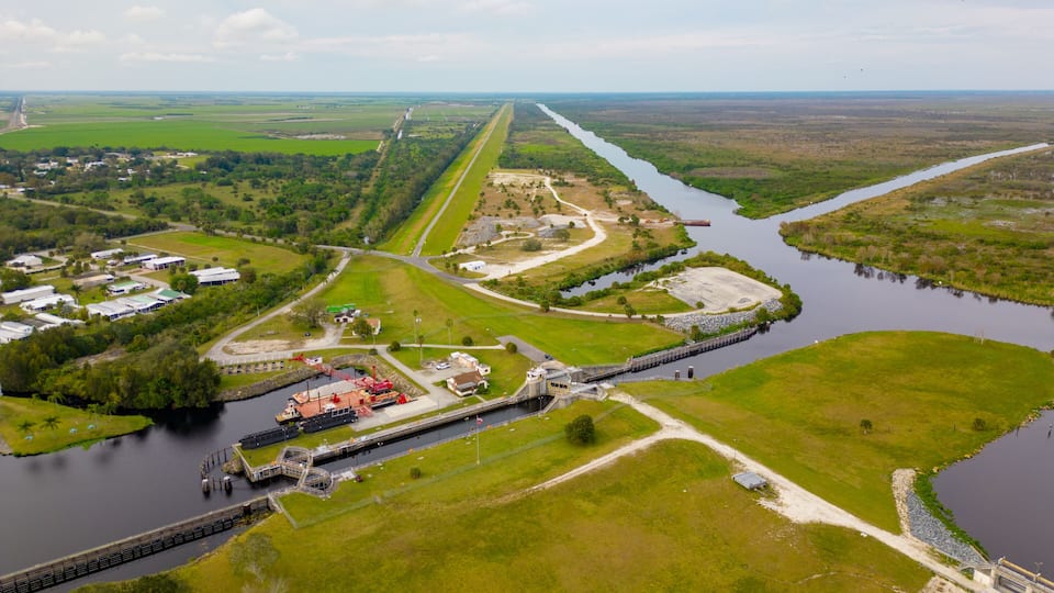 A river with a dam and a bridge, surrounded by green fields and a few buildings.
