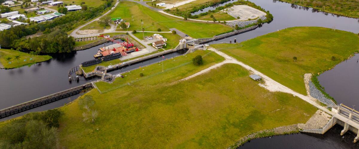 A river with a dam and a bridge, surrounded by green fields and a few buildings.