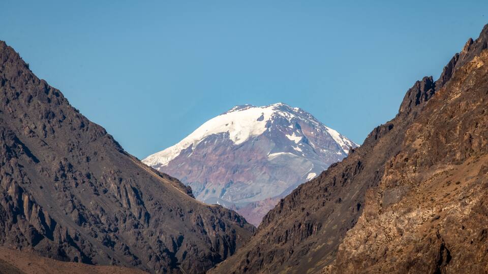 A snow-capped mountain with rocky terrain and a clear blue sky.