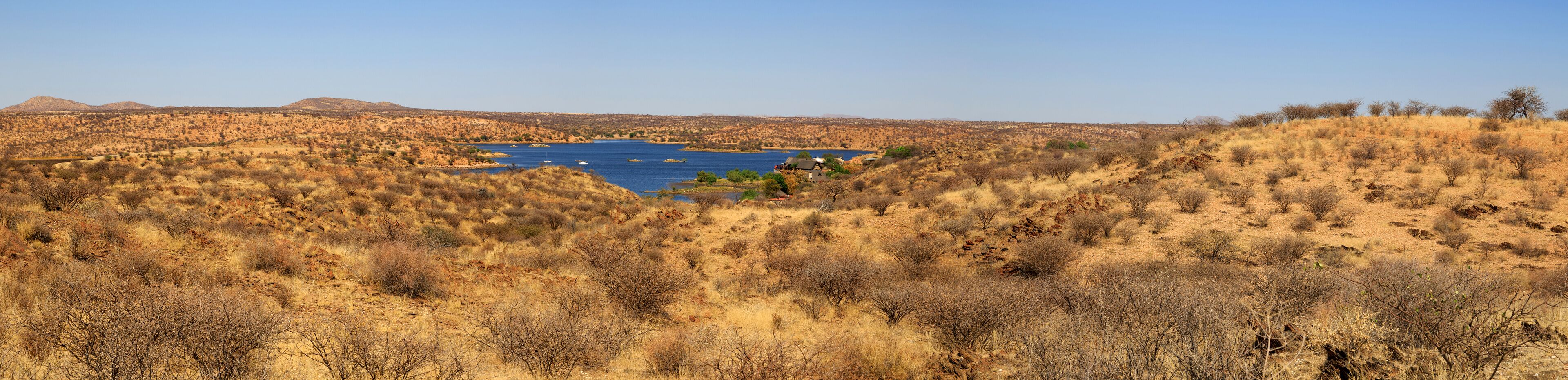 A dry, hilly landscape with sparse vegetation and a large body of water in the center.
