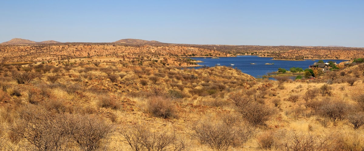 A dry, hilly landscape with sparse vegetation and a large body of water in the center.