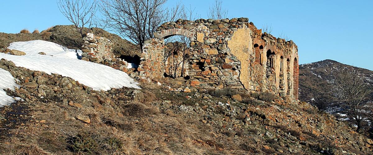 A historic stone ruin on a hillside with snow patches.