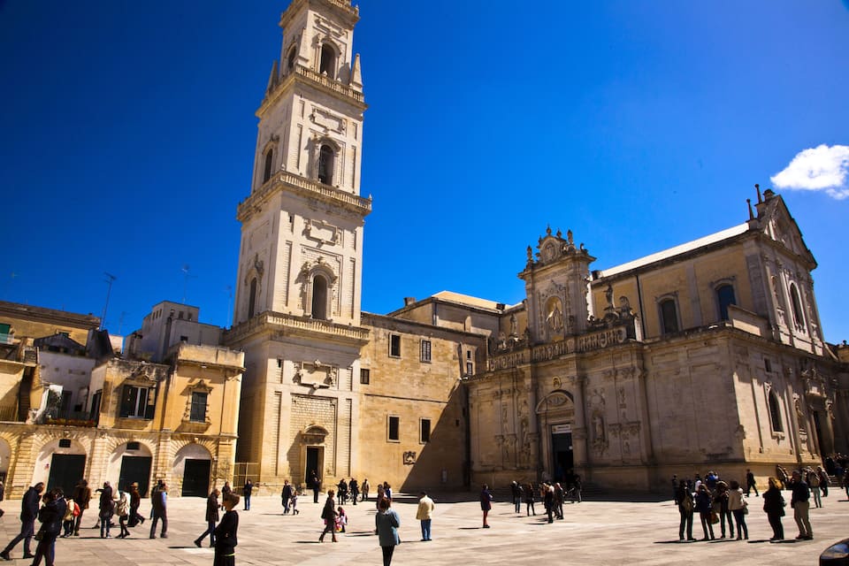 Uma praça histórica com uma torre do relógio imponente e uma catedral.