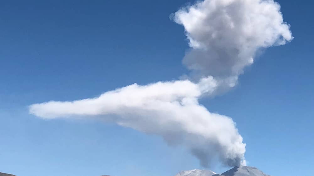Ein Berg, von dessen Spitze eine Rauchwolke aufsteigt.
