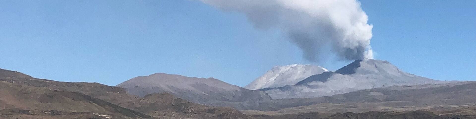 A mountain with a plume of smoke rising from its peak.
