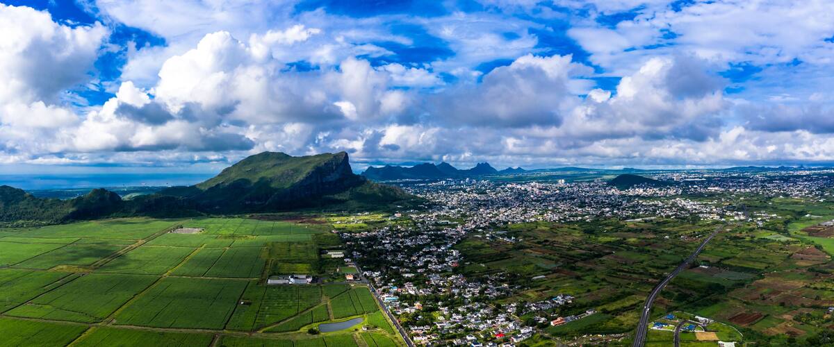 A coastal town with a prominent mountain, green fields, and a clear sky.