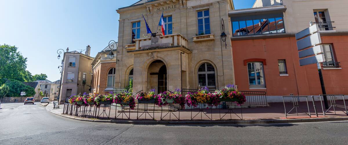 A historic building with a clock tower, French flags, and flower boxes.