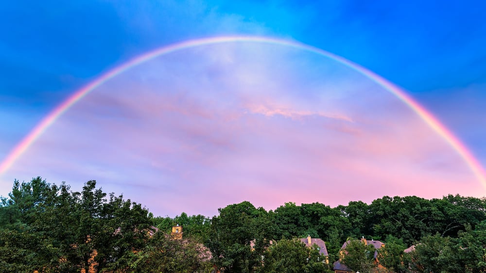 A rainbow arching over a suburban neighborhood with houses and trees.