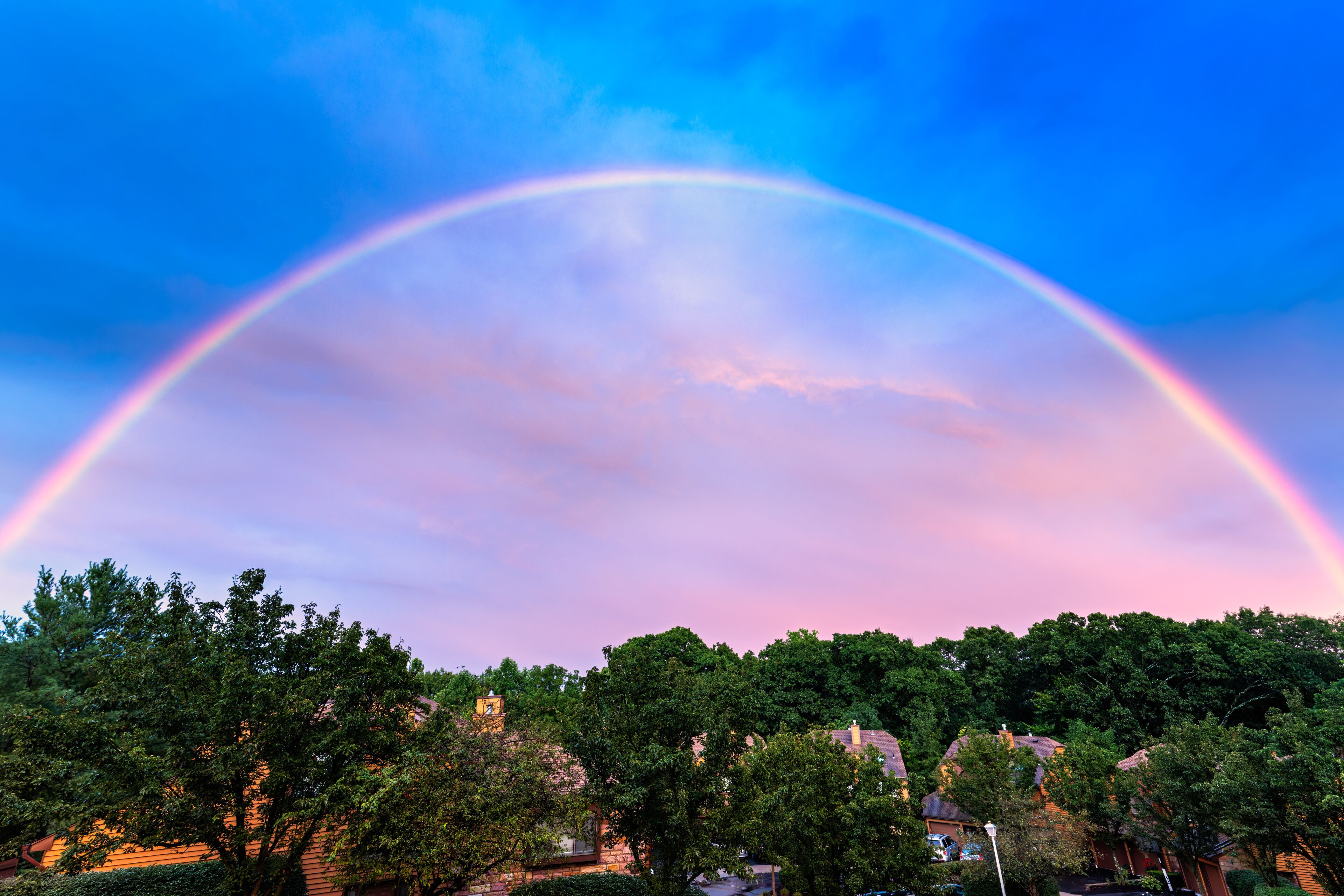 A rainbow arching over a suburban neighborhood with houses and trees.