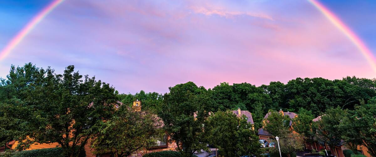 A rainbow arching over a suburban neighborhood with houses and trees.