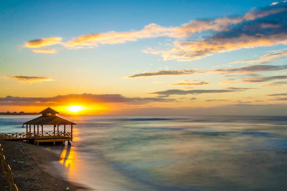 Um pôr do sol sobre uma praia com um gazebo.