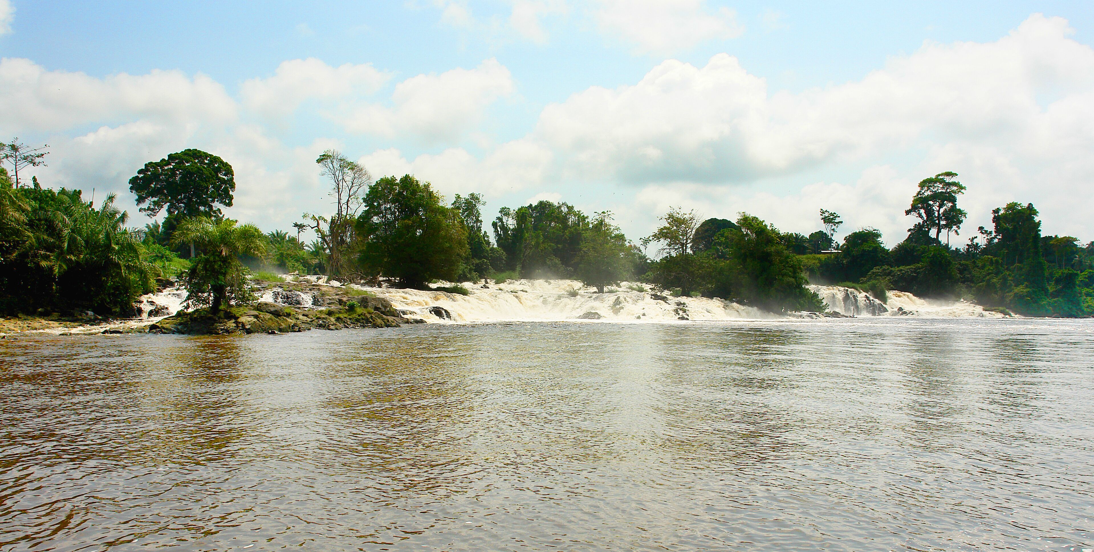 A river with clear water, surrounded by lush greenery and a sandy beach.