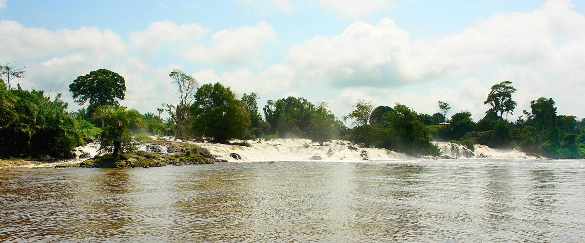 A river with clear water, surrounded by lush greenery and a sandy beach.