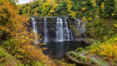 A waterfall cascading into a lake surrounded by autumn foliage.