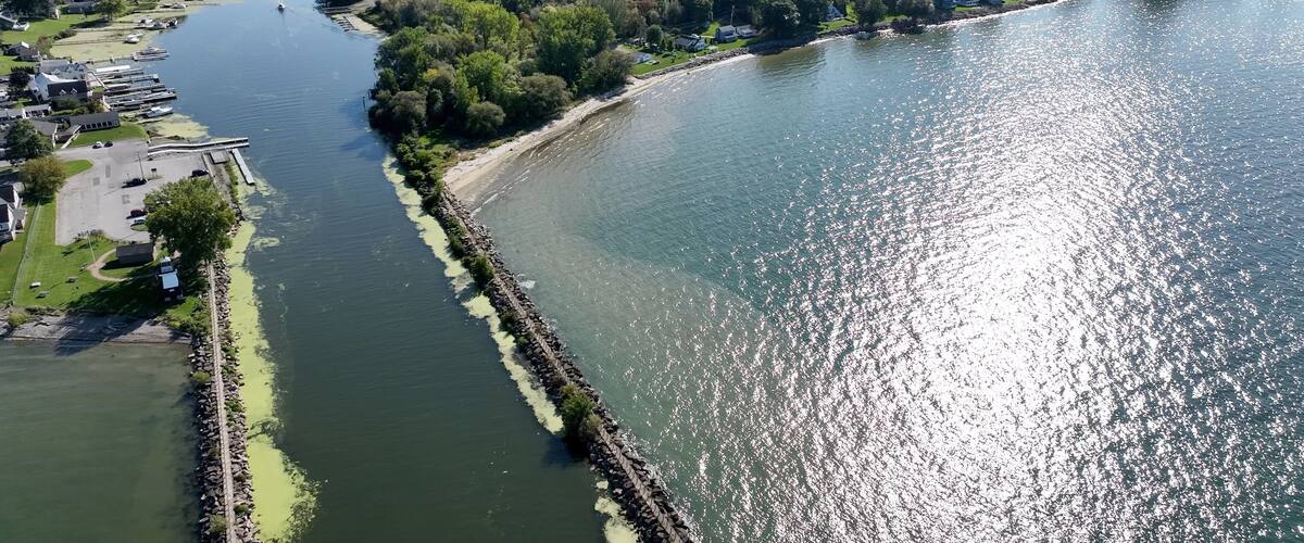 A river with a stone embankment, a marina, and surrounding greenery.