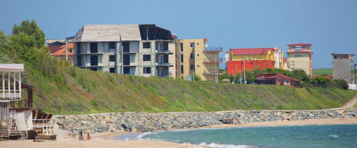 A beach with a rocky shoreline, a wooden structure, and multi-story buildings in the background.