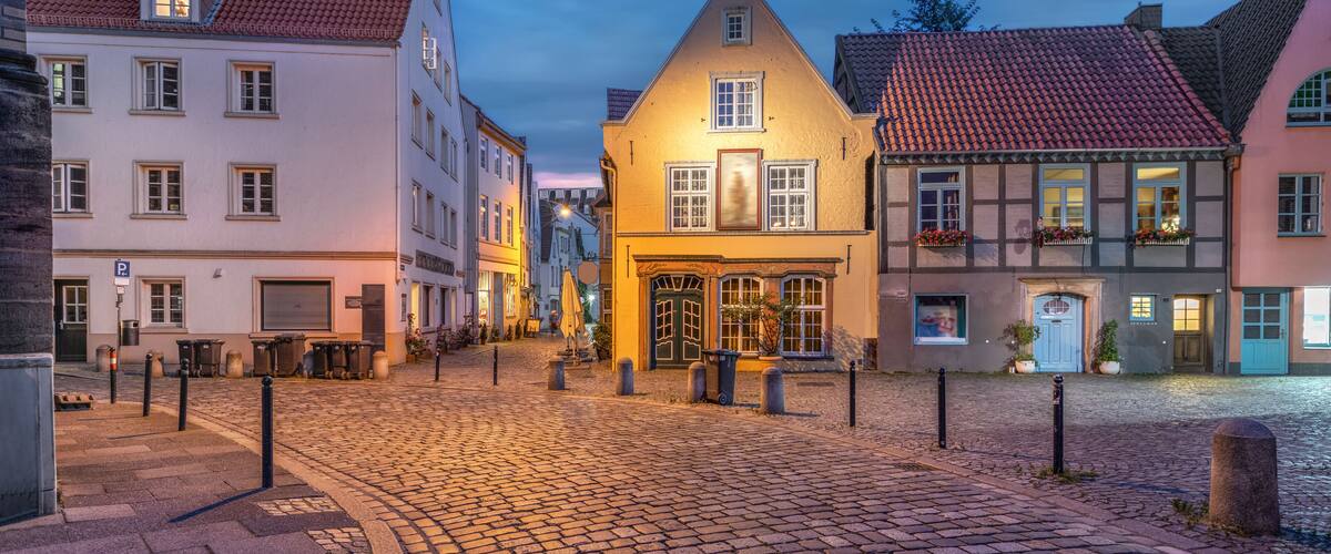 A cobblestone street with historic buildings, a central yellow house, and a traditional European architecture.