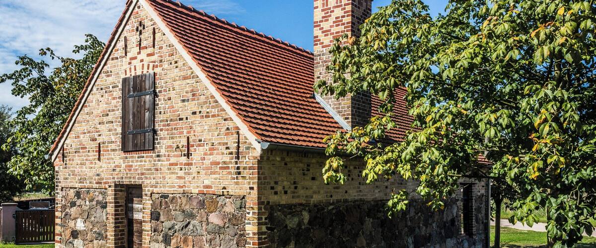 A brick building with a stone foundation, a red-tiled roof, and a chimney.