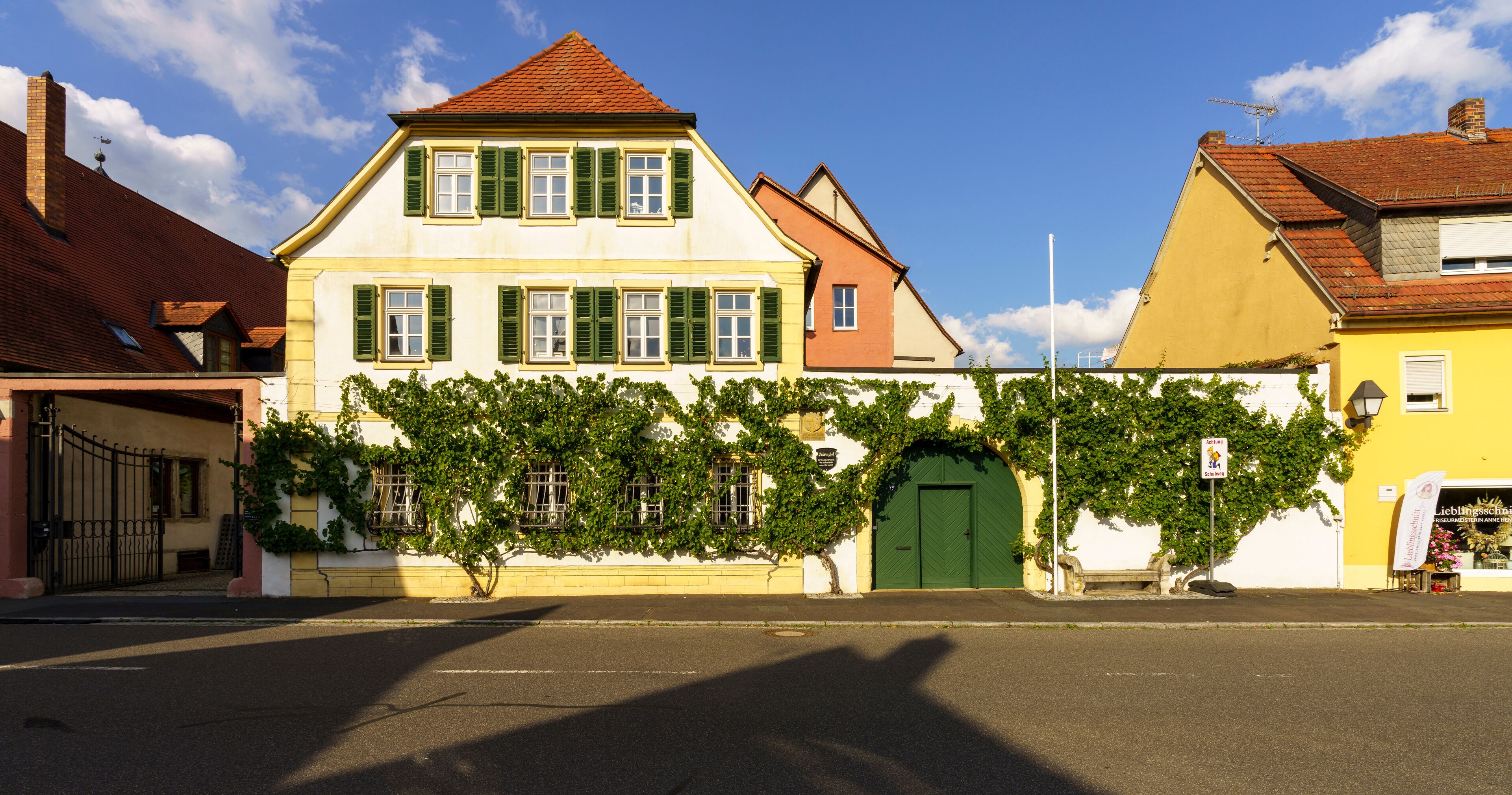 A street with a yellow building, a white building with green shutters, and a green door.