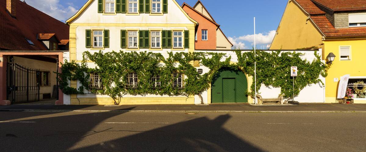 A street with a yellow building, a white building with green shutters, and a green door.