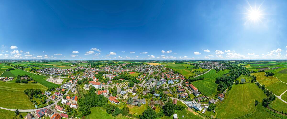 A panoramic view of a town surrounded by green fields and a clear blue sky.