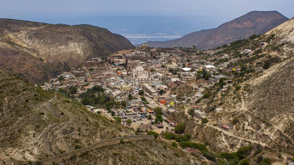 A mountainous town with a prominent church, winding roads, and sparse vegetation.