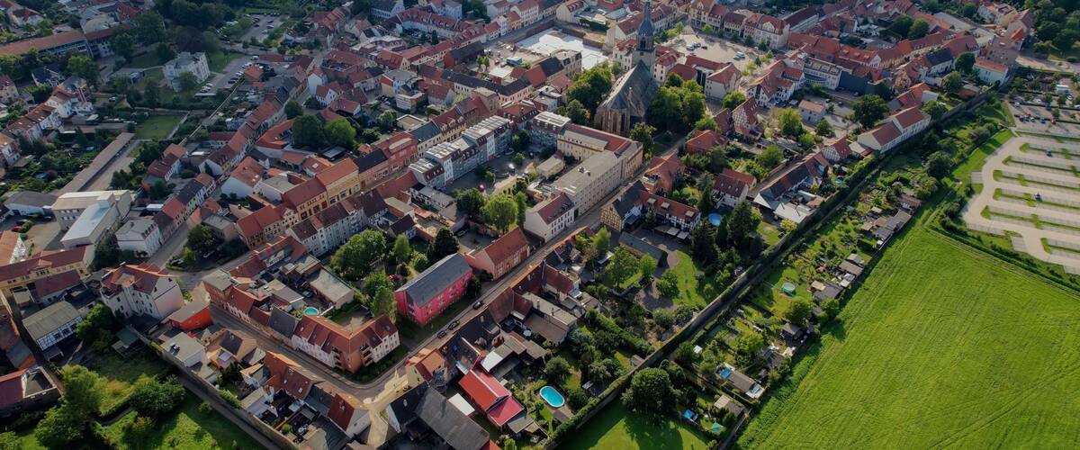 An aerial view of a densely packed residential area with red-roofed houses, a large church, and a sports field.