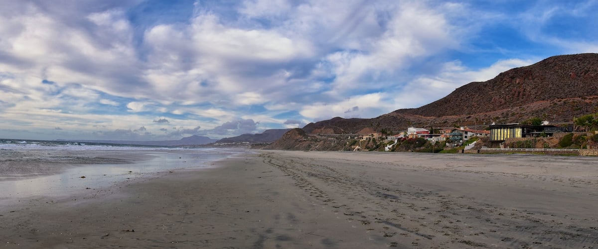 A beach with footprints, a mountain, and houses.