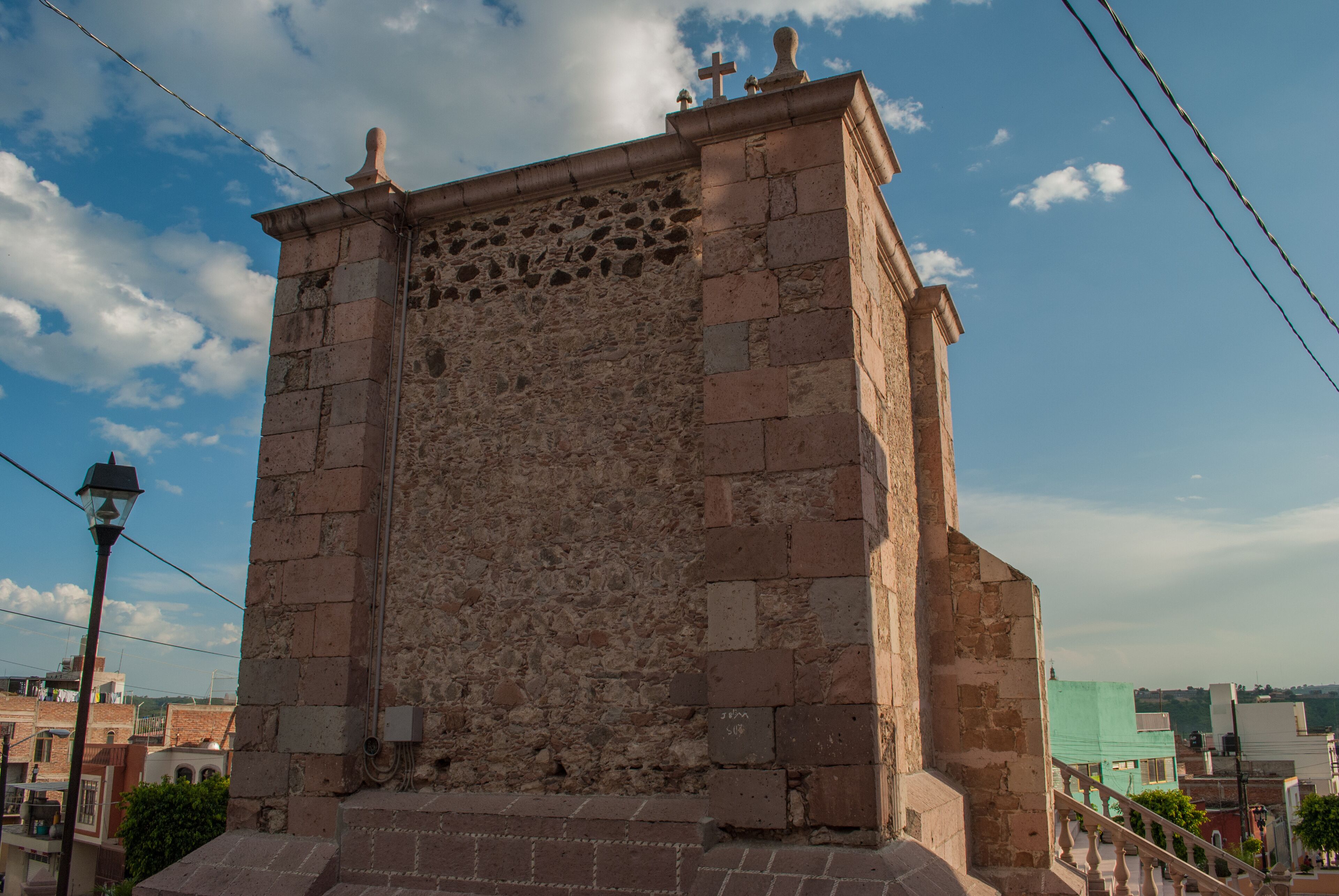A stone tower with a cross on top, surrounded by buildings and a clear sky.