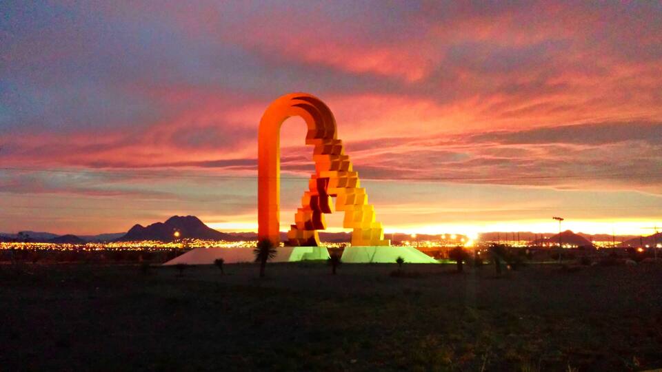 A large, illuminated arch structure in a desert landscape at sunset.