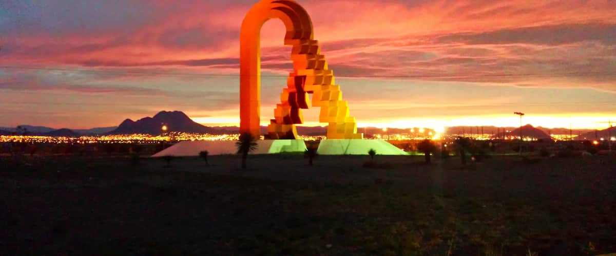 A large, illuminated arch structure in a desert landscape at sunset.
