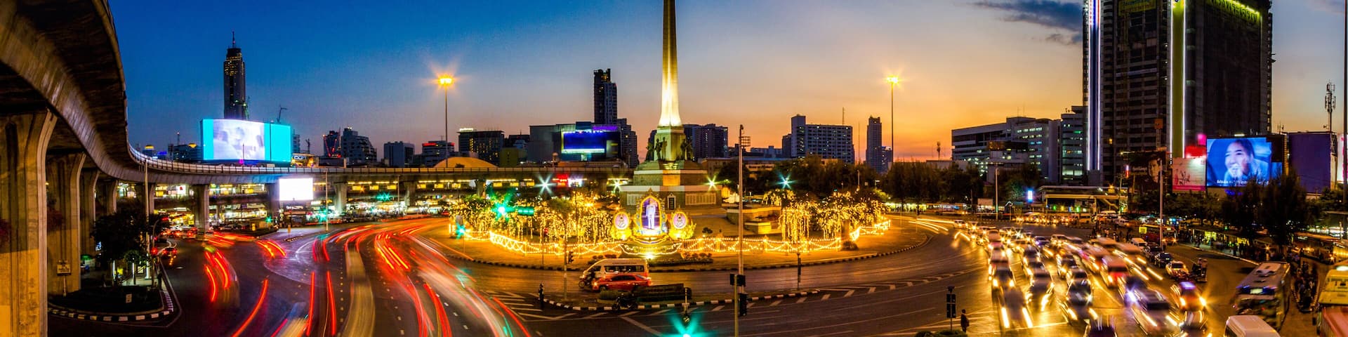 A cityscape at dusk with a prominent monument, busy roads, and illuminated buildings.