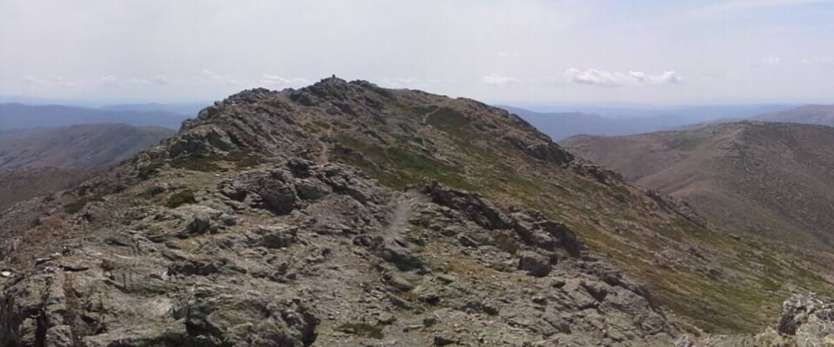 A rugged mountain peak surrounded by other hills and valleys.
