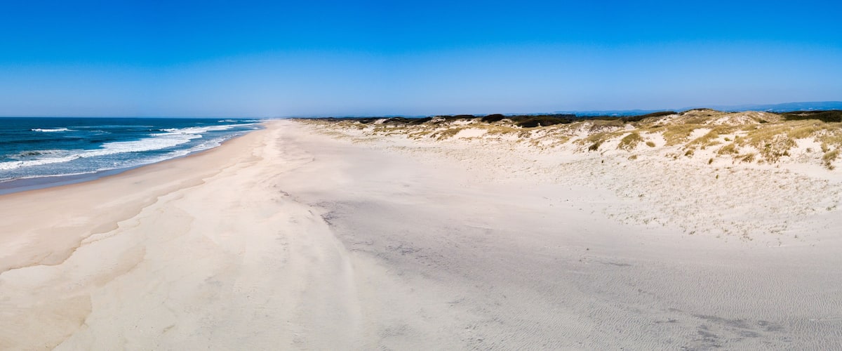 A sandy beach with ocean waves and dunes.
