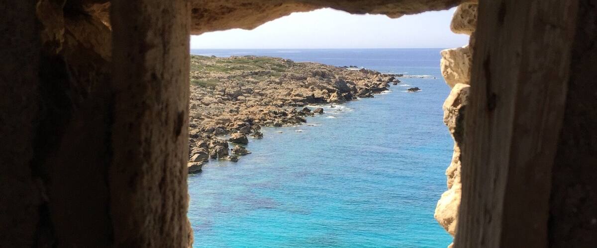 A rocky coastline with a clear blue sea through a stone archway.