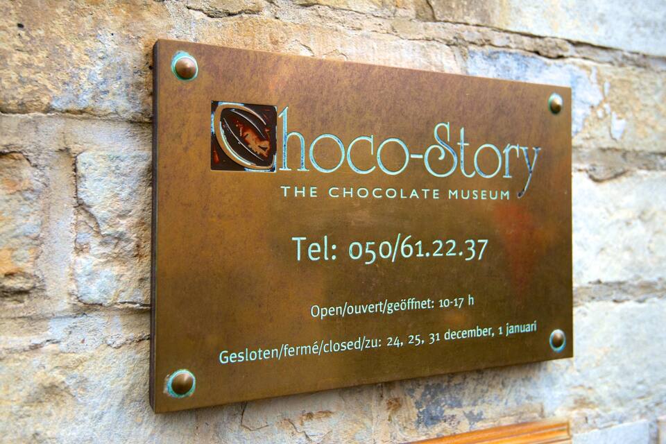 A plaque on a stone wall for Choco-Story, the Chocolate Museum, with contact information and opening hours.