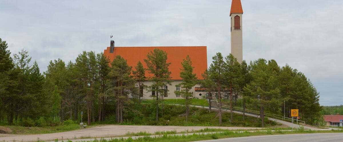A church with a tall tower and a red roof, surrounded by trees.