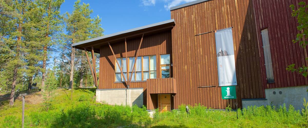 A wooden cabin with a sloped roof, surrounded by dense green forest and a clear blue sky.