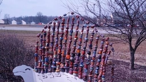 A dinosaur sculpture with a metal body and a fin made from painted chunks of clay.