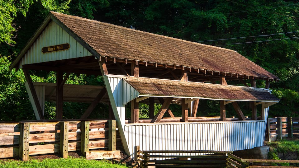 A rustic wooden structure labeled 'Rock Mill' with a metal roof, surrounded by lush greenery.